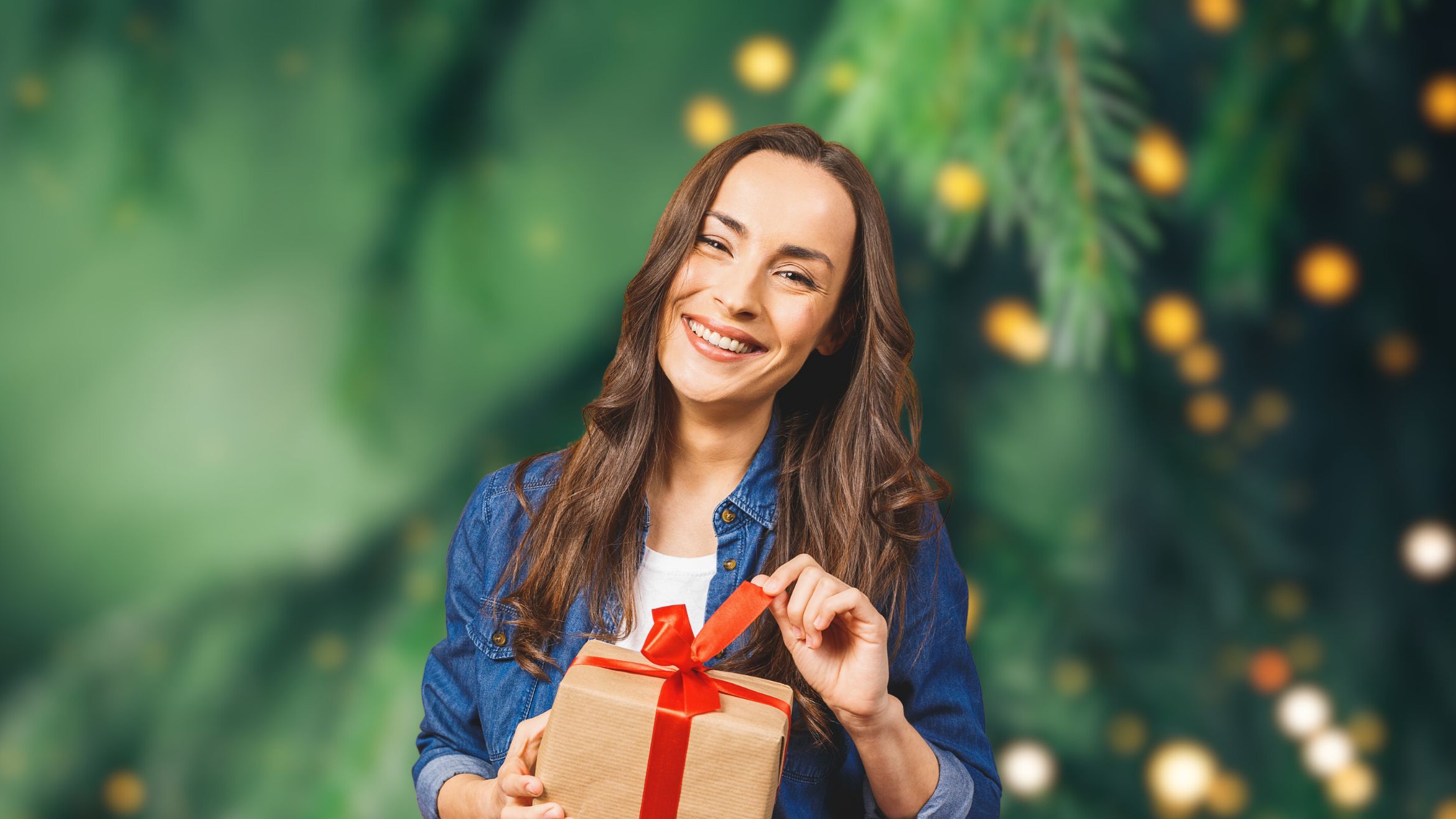 A Happy woman with a present in front of a Christmas tree in the background.